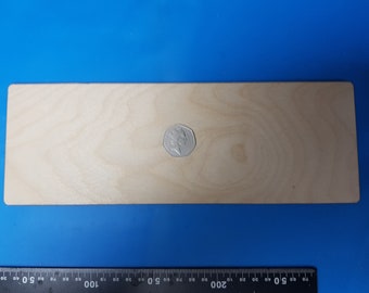 Puede incluir: Una tabla rectangular de madera clara con una moneda encima. La tabla mide aproximadamente 30 cm de largo. Una regla está en la parte inferior de la imagen, con medidas en centímetros.