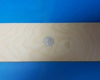 Puede incluir: Una pieza rectangular de madera sin terminar con veta de madera natural. Una moneda se coloca en el centro de la madera.
