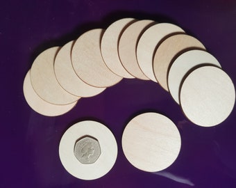 May include: A group of 12 unfinished wooden circles, arranged in a semi-circle, with two additional circles below. The circles are approximately 2 inches in diameter. A British coin is placed on one of the circles for size comparison.