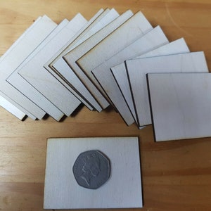 May include: A selection of small, unfinished wooden squares and L-shaped pieces. The wood is a light, natural colour with visible grain. A fifty pence coin is placed on one of the wooden squares for size comparison. Ideal for crafting or DIY projects.