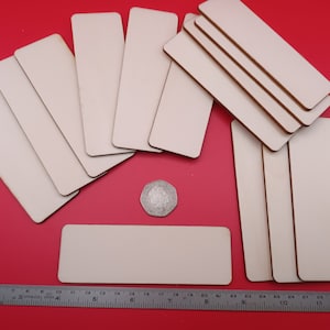 May include: A set of 14 unfinished wooden rectangular plaques, approximately 7.6 cm by 17.8 cm, arranged on a red surface. A ruler and a coin are included for size reference.