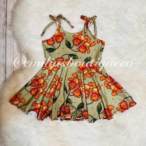 May include: A green and orange sleeveless dress with a teddy bear print. The dress has a ruffled hem and tie straps.
