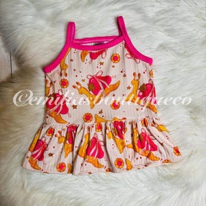 May include: A pink and white sleeveless dress with a ruffled hem. The dress has a pattern of snails with pink and yellow accents. The straps of the dress are pink.