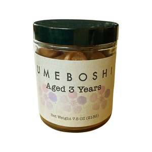 May include: A glass jar with a black lid filled with brown umeboshi plums. The label reads "UMEBOSHI Aged 3 Years" and "Net Weight 7.5 OZ (213G)".