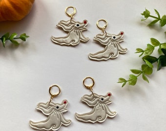 May include: A pair of white, ghost-shaped earrings with red and black details. The earrings are on a white background.