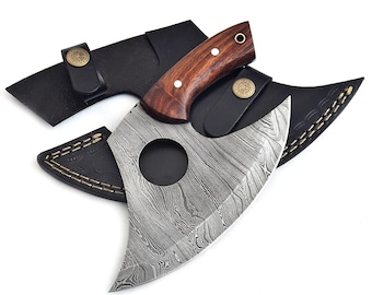 May include: A Damascus steel cleaver with a dark wood handle and a black leather sheath. The blade has a unique pattern and a circular cutout. The handle is secured with two rivets. The sheath has a snap closure.