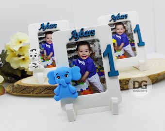 May include: Three white photo frames with blue accents and a blue elephant figurine. Each frame has a photo of a young boy and the name "Aybars" written on the top. The number "1" is displayed on the front of each frame.