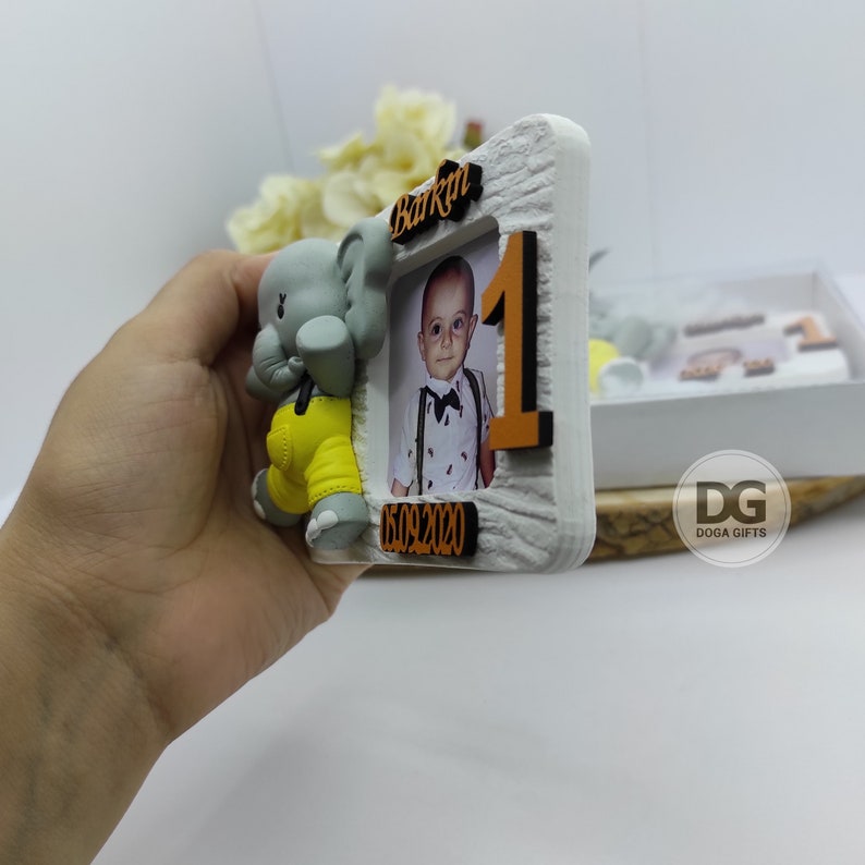 May include: A white wooden photo frame with a gray elephant figurine. The frame has a photo of a young boy and the text "Barkan 05.09.2020".