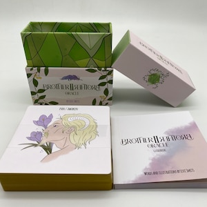 May include: A set of Brother II Rentory Oracle cards in a green and white box with a guidebook. The cards feature illustrations of a person with horns and flowers. The box has the text "Brother II Rentory Oracle" and "By Levi Smits". The guidebook has the text "Brother II Rentory Oracle Guidebook" and "Words and Illustrations by Levi Smits".