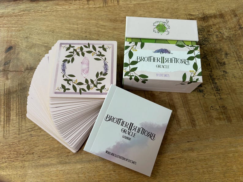 May include: A deck of Brother II Brother Grace Oracle cards with a pink and green floral design. The cards are fanned out and the box is closed. The box is white with green and pink floral designs and the text "Brother II Brother Grace Oracle" in black.