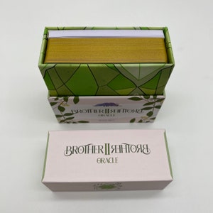 May include: A box of Brother II Brother Oracle cards with a green and white geometric pattern on the top and a pink box with the text "Brother II Brother Oracle" on the front.
