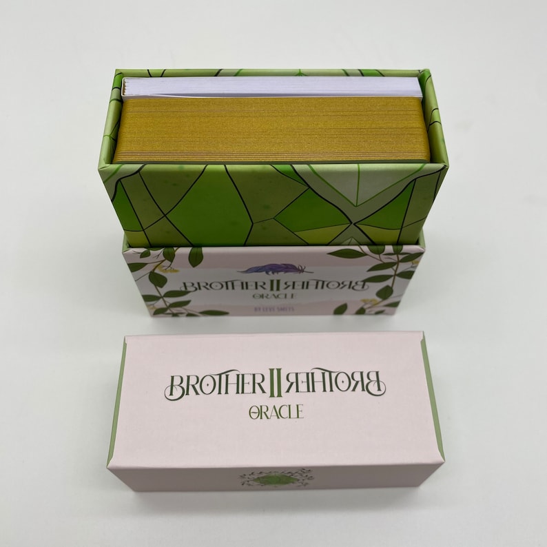 May include: A box of Brother II Brother Oracle cards with a green and white geometric pattern on the top and a pink box with the text "Brother II Brother Oracle" on the front.
