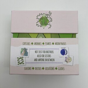 May include: A pink box with a green crystal design on the top and a green and white geometric pattern on the bottom. The box contains cards with illustrations of crystals, animals, plants, moon phases, seasons, deities, locations, and guides. The text on the box reads "Not just for brothers also for sisters and anyone in between."