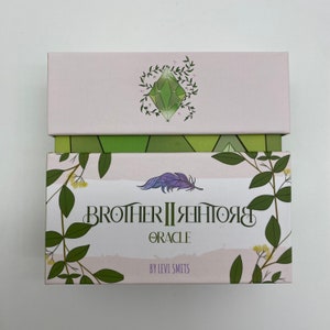 May include: A box for the Brother II Brother Oracle deck. The box is pink with green foliage and a green crystal design. The text on the box reads "Brother II Brother Oracle" and "By Levi Smits".