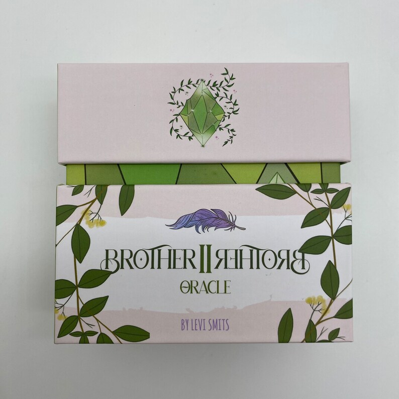 May include: A box for the Brother II Brother Oracle deck. The box is pink with green foliage and a green crystal design. The text on the box reads "Brother II Brother Oracle" and "By Levi Smits".