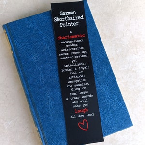 May include: Black bookmark with white text describing the German Shorthaired Pointer breed. The text reads "a charismatic medium-sized gundog; aristocratic; never grows up; scatter-brained yet intelligent; loving & loyal; full of attitude; energetic; the sassiest thing on four legs; a crazy weirdo who will make you laugh all day long". A red heart is at the bottom of the bookmark.