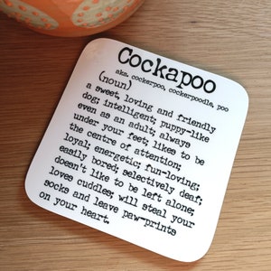 May include: A white coaster with black text defining a Cockapoo as a "sweet, loving and friendly dog". The text also describes the dog as "intelligent, puppy-like, always under your feet, likes to be the centre of attention, loyal, energetic, fun-loving, easily bored, selectively deaf, doesn't like to be left alone, loves cuddles, will steal your socks and leave paw prints on your heart."