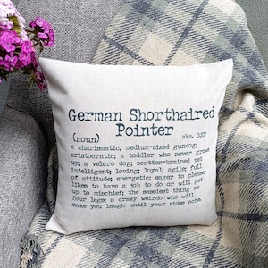 May include: A beige cushion with a black and white graphic print that defines a German Shorthaired Pointer. The text reads "German Shorthaired Pointer (noun) aka. GSP a charismatic, medium-sized gundog; aristocratic; a toddler who never grows up; a velcro dog; scatter-brained yet intelligent; loving; loyal; agile; full of attitude; energetic; eager to please; likes to have a job to do or will get up to mischief; the sassiest thing on four legs; a crazy weirdo who will make you laugh until your sides ache."
