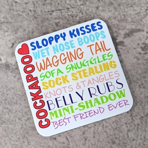 May include: A white square coaster with colourful text that reads "Cockapoo Sloppy Kisses Wet Nose Boops Wagging Tail Sofa Snuggles Sock Stealing Knots & Tangles Belly Rubs Mini-Shadow Best Friend Ever".