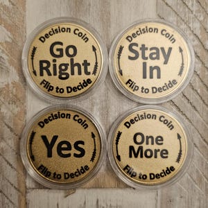 May include: Four gold-colored decision coins with black text. Each coin is in a clear plastic case. The coins say "Go Right", "Stay In", "Yes", and "One More". Each coin has the text "Decision Coin" and "Flip to Decide".