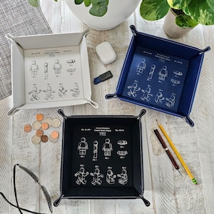 May include: Three different colored felt trays with a white outline. Each tray features a black and white illustration of a LEGO person with the text "LEGO PERSON United States Patent" and the patent number. The trays are on a light wood surface.
