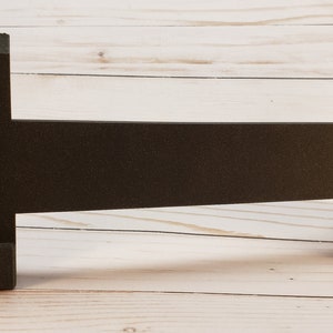 Puede incluir: Un soporte de espuma negro con dos extremos curvos y una larga secci&oacute;n central plana. El soporte est&aacute; dise&ntilde;ado para sostener un par de auriculares.