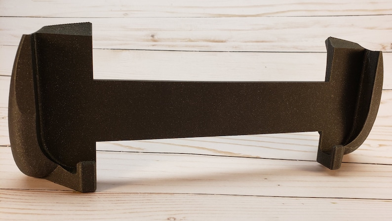 Puede incluir: Un soporte de espuma negro con dos extremos curvos y una larga secci&oacute;n central plana. El soporte est&aacute; dise&ntilde;ado para sostener un par de auriculares.