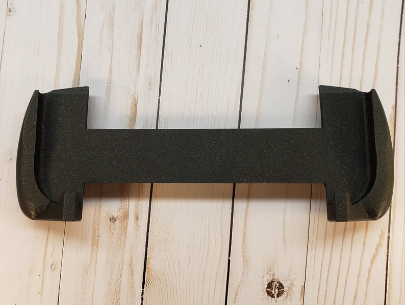Puede incluir: Soporte para tel&eacute;fono de pl&aacute;stico negro con un dise&ntilde;o curvo. El soporte est&aacute; dise&ntilde;ado para sostener un tel&eacute;fono en posici&oacute;n vertical.