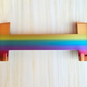Puede incluir: Un soporte de metal de color arco&iacute;ris con un acabado dorado. El soporte est&aacute; dise&ntilde;ado para sostener un estante u otro objeto.