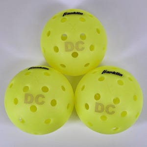 May include: Three yellow pickleball balls with black "Franklin" and "DC" lettering. The balls have a dimpled surface.