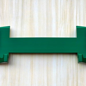 Puede incluir: Un soporte para tel&eacute;fono de pl&aacute;stico verde con dos extremos curvos para sujetar un tel&eacute;fono en su lugar.