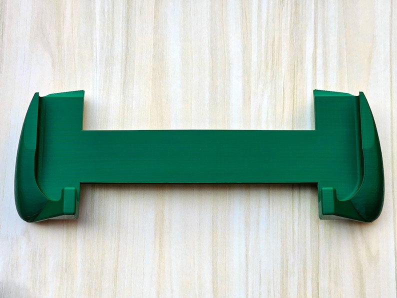 Puede incluir: Un soporte para tel&eacute;fono de pl&aacute;stico verde con dos extremos curvos para sujetar un tel&eacute;fono en su lugar.