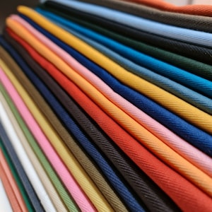 May include: A collection of fabric swatches in various colors, including red, orange, yellow, green, blue, and pink. The fabric is folded and arranged in a fan shape, showcasing the different colors and textures.