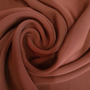 May include: Close-up of a deep red fabric with a soft, smooth texture. The fabric is folded and draped, creating a swirling pattern.