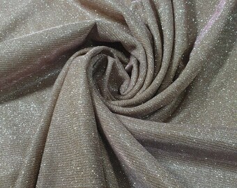 May include: Close-up of a shimmery, light brown fabric with a subtle sparkle. The fabric is folded and draped, creating a soft, flowing texture.
