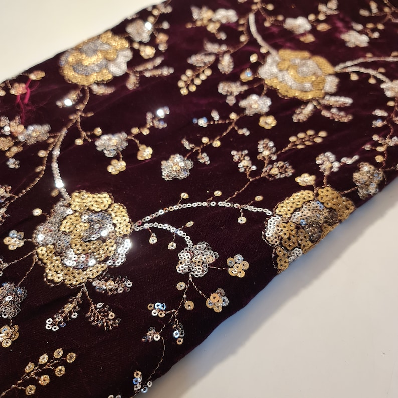 May include: Burgundy velvet fabric with gold and silver sequins in a floral pattern.