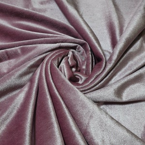 May include: Close-up of a soft, pink velvet fabric with a subtle shimmer. The fabric is draped and folded, creating a luxurious and elegant look.