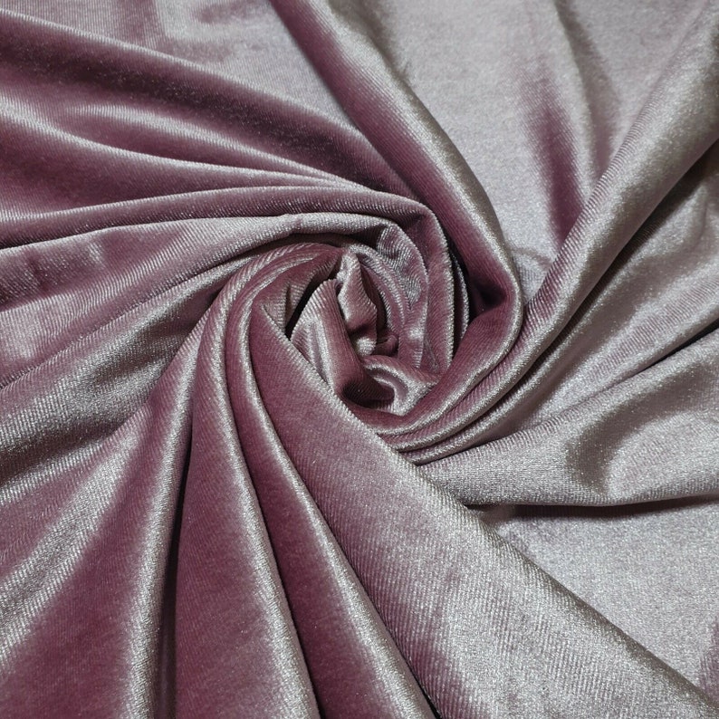 May include: Close-up of a soft, pink velvet fabric with a subtle shimmer. The fabric is draped and folded, creating a luxurious and elegant look.