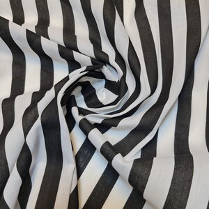 May include: Black and white striped fabric with a diagonal pattern. The fabric is folded and draped, showing the texture and weave.