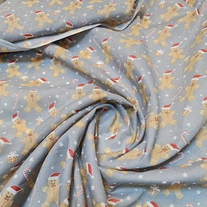 May include: A grey fabric with a repeating pattern of gingerbread men wearing red Santa hats. The gingerbread men are holding candy canes and gifts. The fabric is ideal for Christmas crafts and projects.