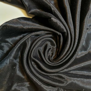 May include: Black satin fabric with a smooth, silky texture. The fabric is draped and folded, creating a swirling pattern.