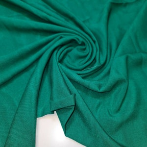 May include: A close-up of a smooth, emerald green fabric. The fabric is draped and folded, creating a soft, flowing texture.