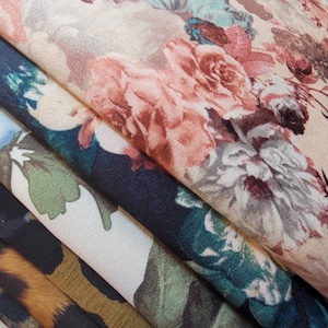 May include: A stack of fabric swatches with floral patterns. The top swatch is a light beige with pink and white flowers. The second swatch is a dark blue with green and white flowers. The third swatch is a light beige with green and brown flowers. The bottom swatch is a brown and orange animal print.