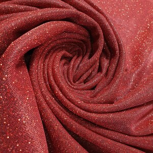Puede incluir: Tela roja brillante con un patrón texturizado y tejido. La tela está doblada y retorcida en forma de espiral.