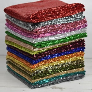 Può includere: Una pila di 12 tessuti di paillettes di diversi colori. I tessuti sono tutti della stessa dimensione e sono impilati uno sopra l'altro. I colori dei tessuti sono rosso, argento, rosa, bianco, verde, beige, bordeaux, blu, oro, verde oliva, turchese e grigio.