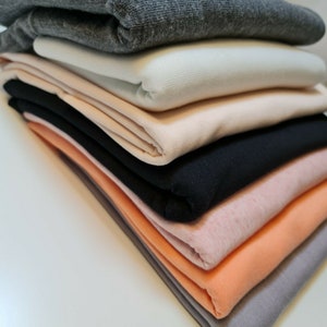 May include: A stack of fabric swatches in various colors, including gray, white, peach, black, pink, and orange. The fabric is folded neatly and appears to be soft and comfortable.