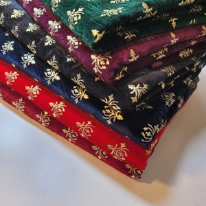 May include: A stack of six velvet fabric swatches with a gold floral pattern. The fabrics are in various colors, including green, purple, black, and red.