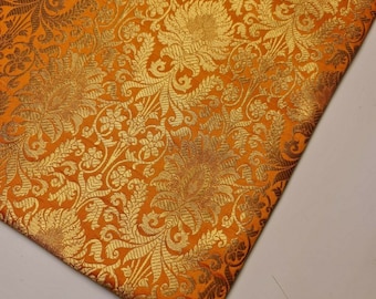 Könnte beinhalten: Orangener Stoff mit einem goldenen Brokatmuster aus floralen Designs. Der Stoff hat einen dezenten Glanz und ein luxuriöses Gefühl.