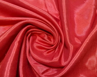 May include: Close-up of a smooth, red fabric with a soft, silky texture. The fabric is draped and folded, creating a swirling pattern.