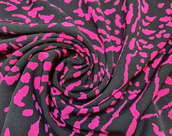 Puede incluir: Tela negra con estampado abstracto rosa. La tela está doblada y drapeada, mostrando la textura y el patrón.